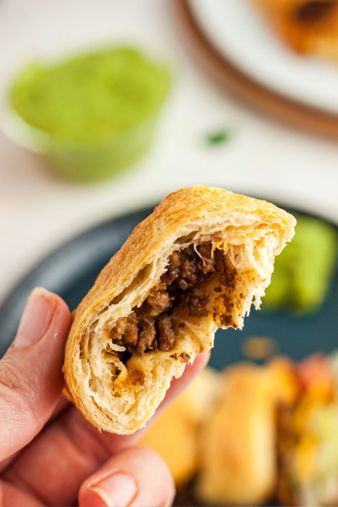 Hand holding a bite of taco ring showing flaky crescent roll around taco meat and cheese.