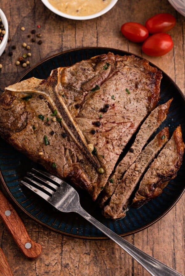 Juicy steak on a blue plate with sauce, fork, and knives on the table