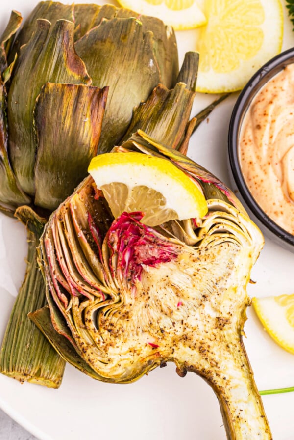 Air fryer artichoke on a white plate with a side of dipping sauce.