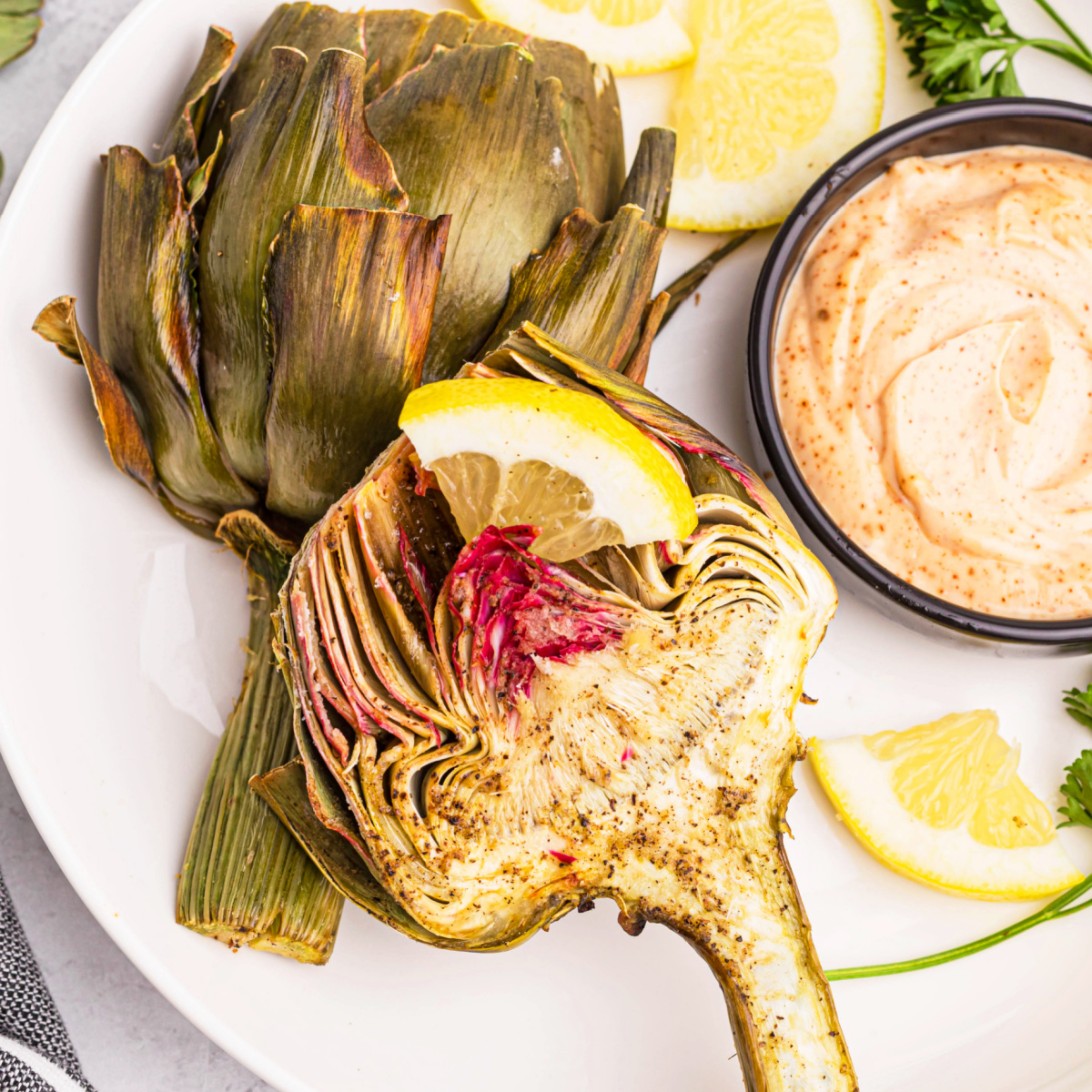 Air fryer artichoke on a white plate with a side of dipping sauce.