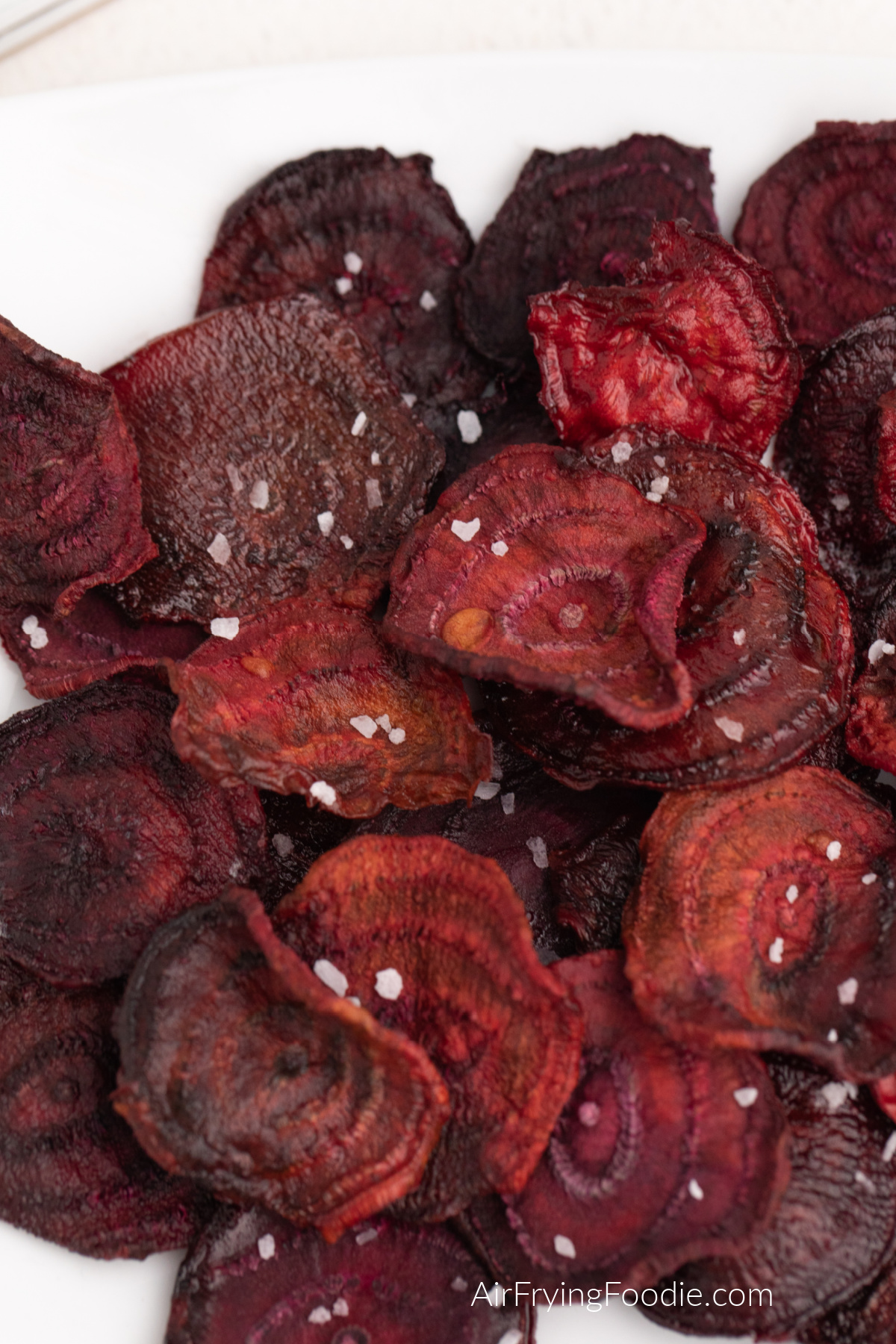 Close up photos of air fried beet chips on a white plate and topped with kosher salt. 