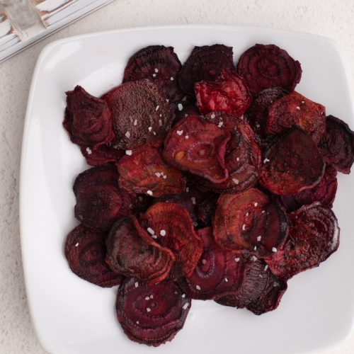 Overhead shot pf beet chips made in the air fryer, served on a whote plate, and topped with kosher salt.