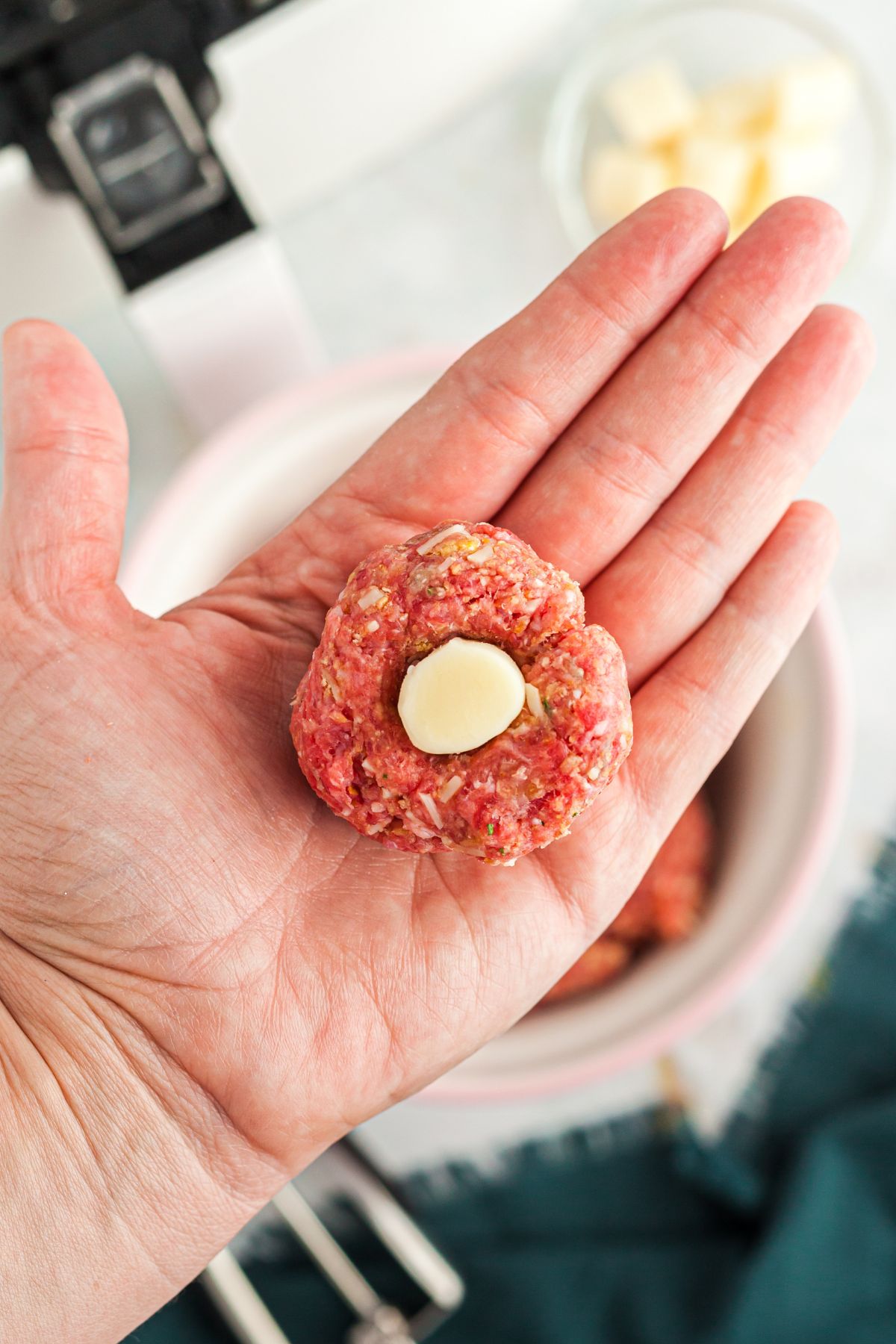 Raw meatball in a hand with a piece of cheese being stuffed into the meat.