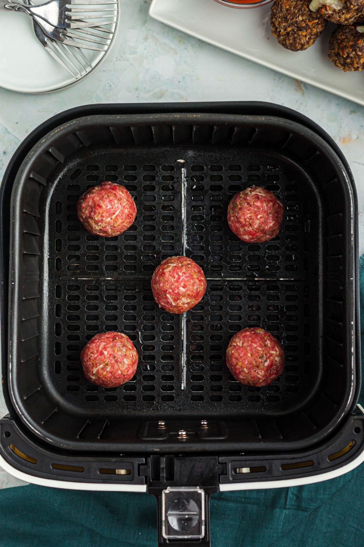Uncooked meatballs rolled and placed in the air fryer basket.