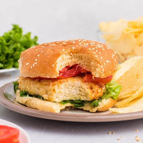 Chicken burger with lettuce and tomato and served with chips, missing a bite.