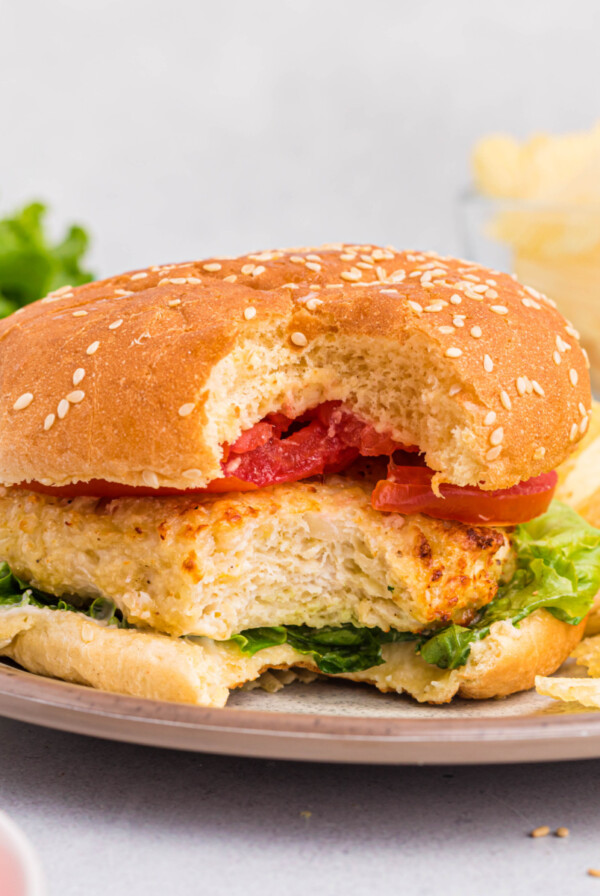 Chicken burger with lettuce and tomato and served with chips, missing a bite.