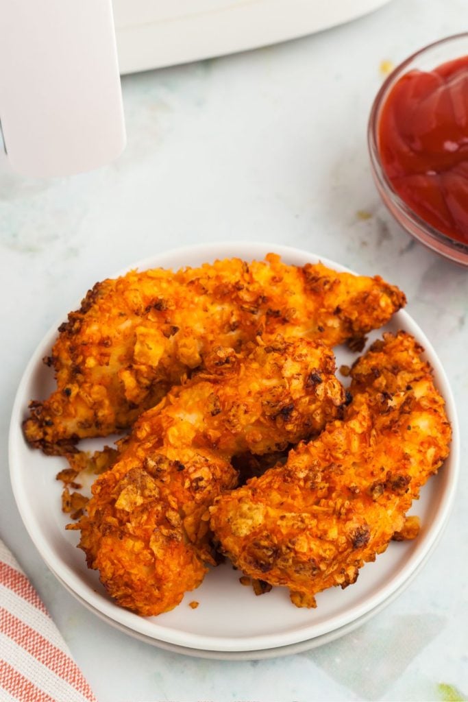 Three dorito coated chicken strips on a white plate 