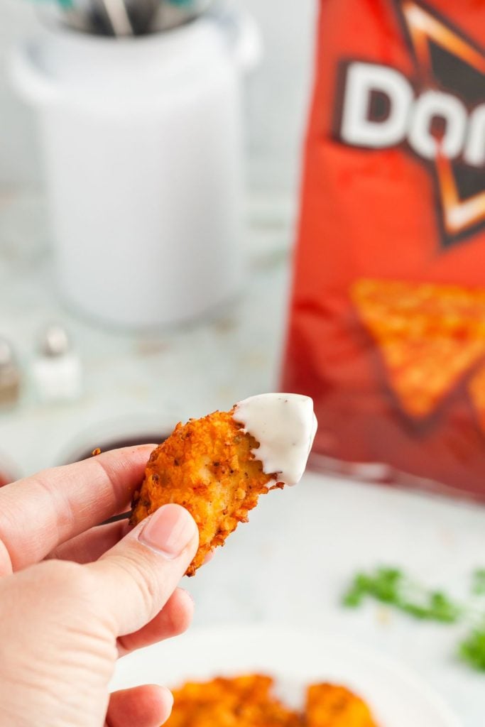 Chicken tender dipped in ranch with dorito bag in background
