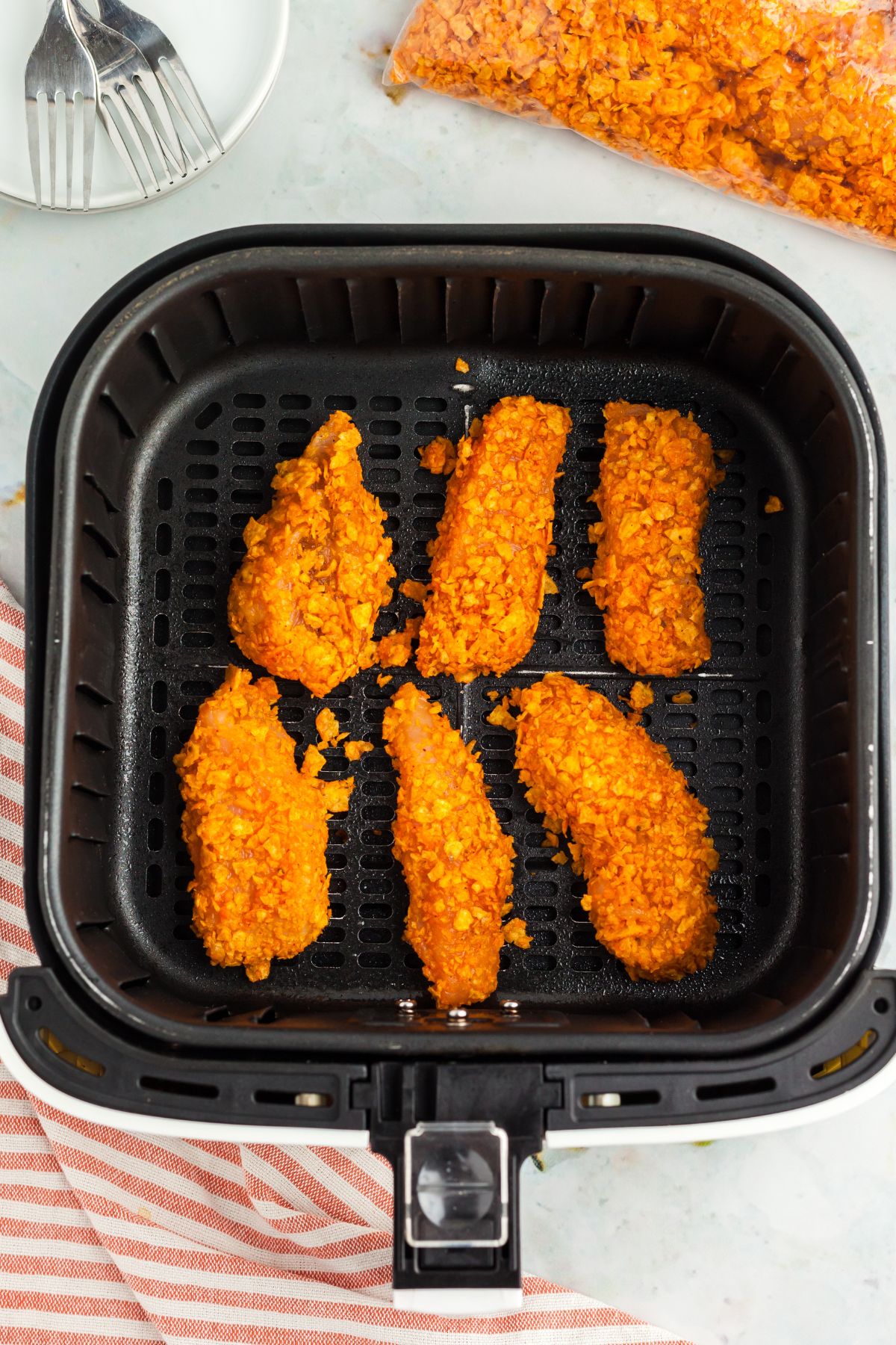 Chicken strips coated with crushed dorito chips in the air fryer basket