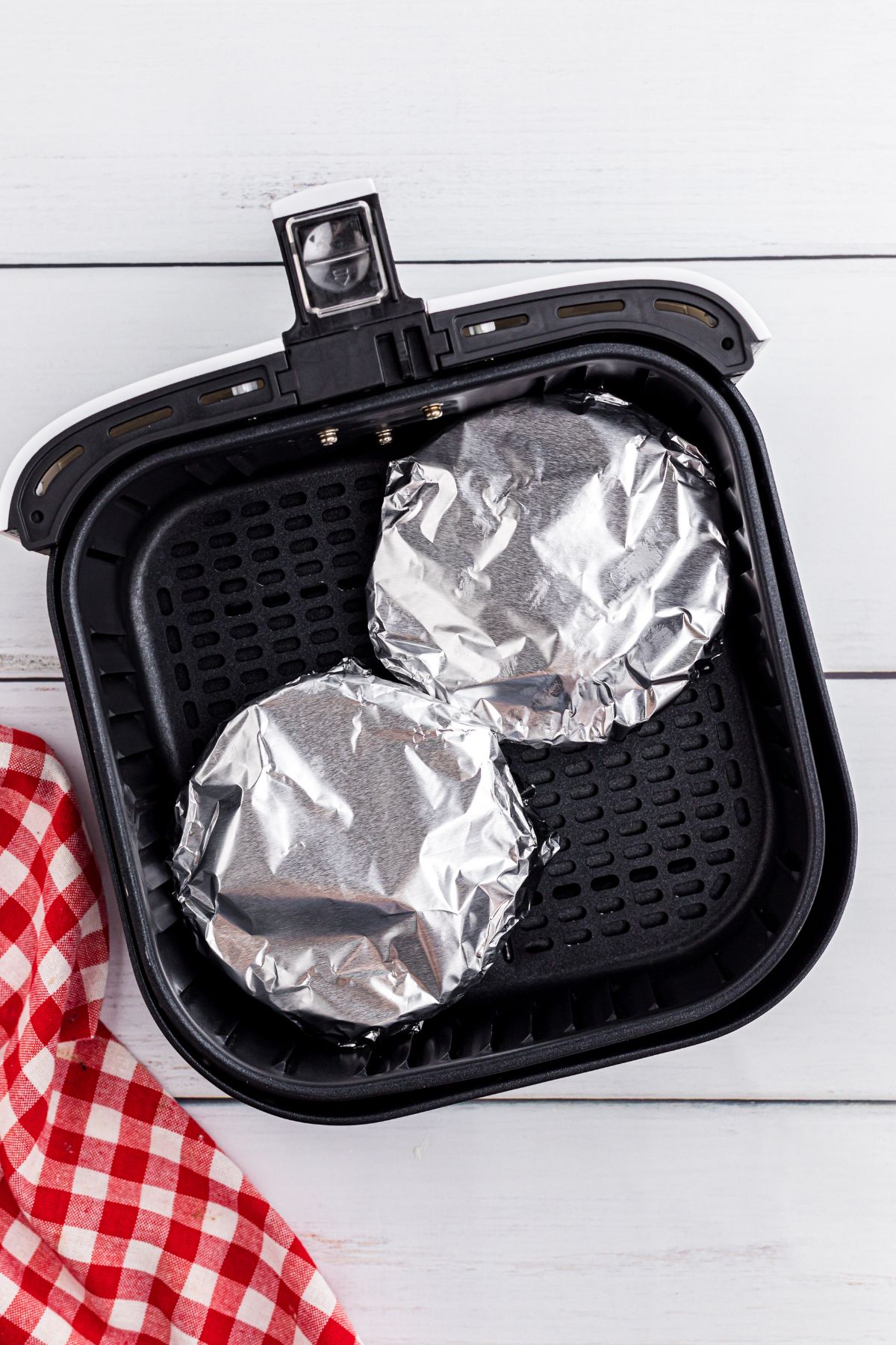 Pot pies covered in foil in an air fryer basket.
