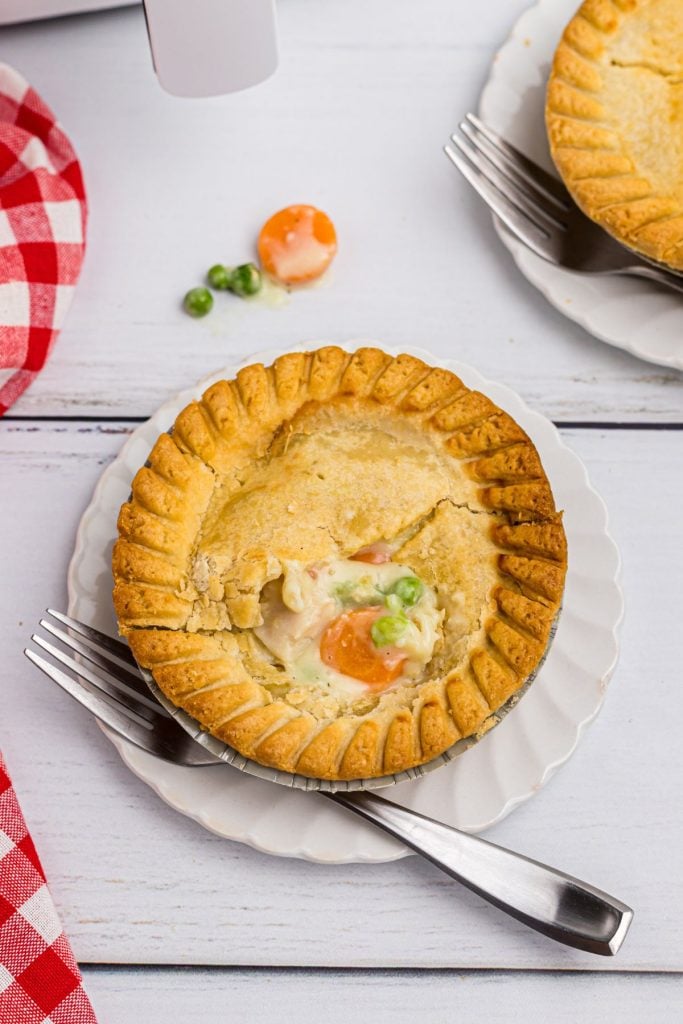 Golden pot pie on a white board with a fork and dishcloth on the table