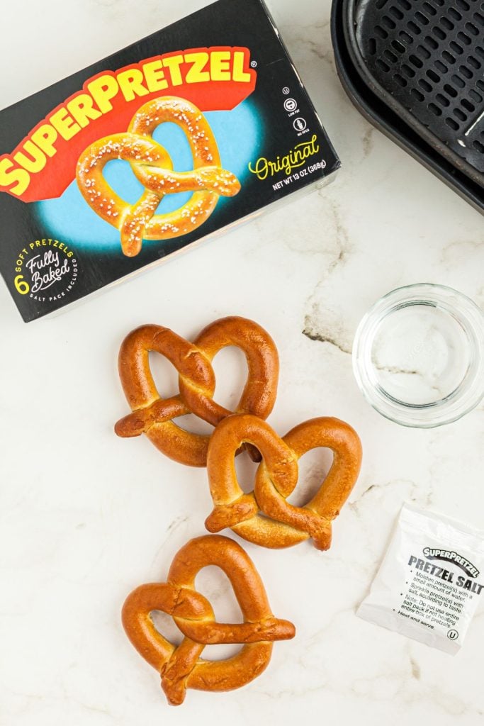 Frozen pretzels and the box with salt on a marble table in front of an air fryer basket. 