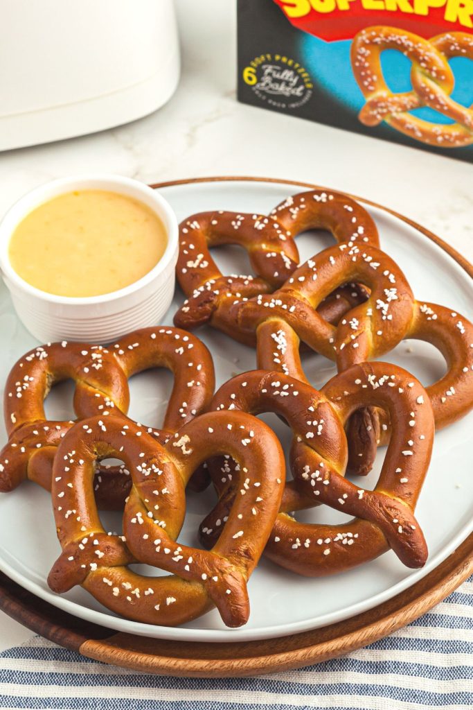 Golden pretzels on a white plate with nacho cheese on the plate. 