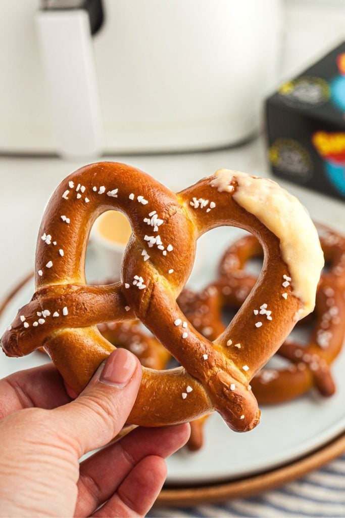 Hand holding golden brown pretzel dipped in cheddar cheese.