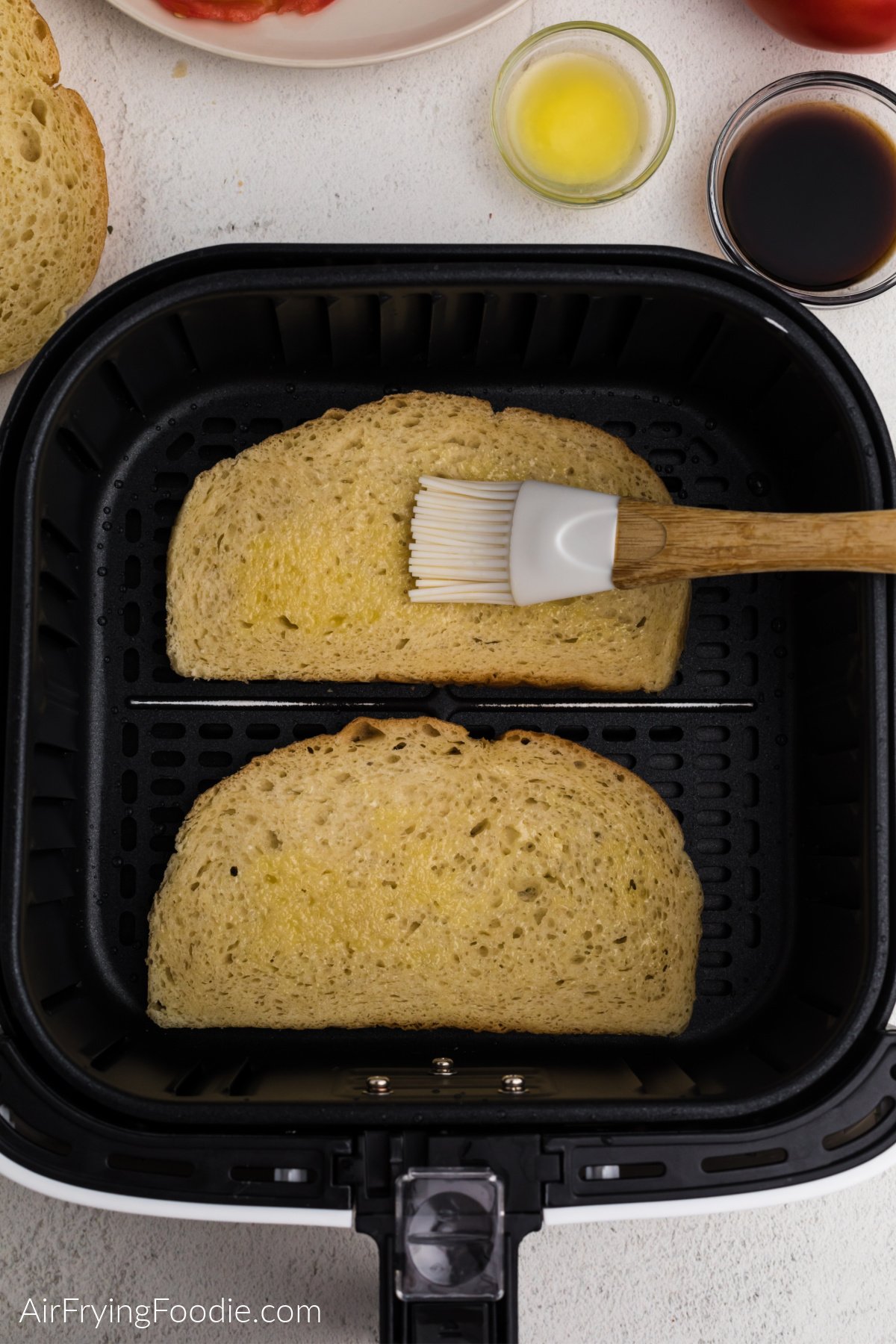 Brushing a light coat of butter onto sourdough bread in the air fryer basket.
