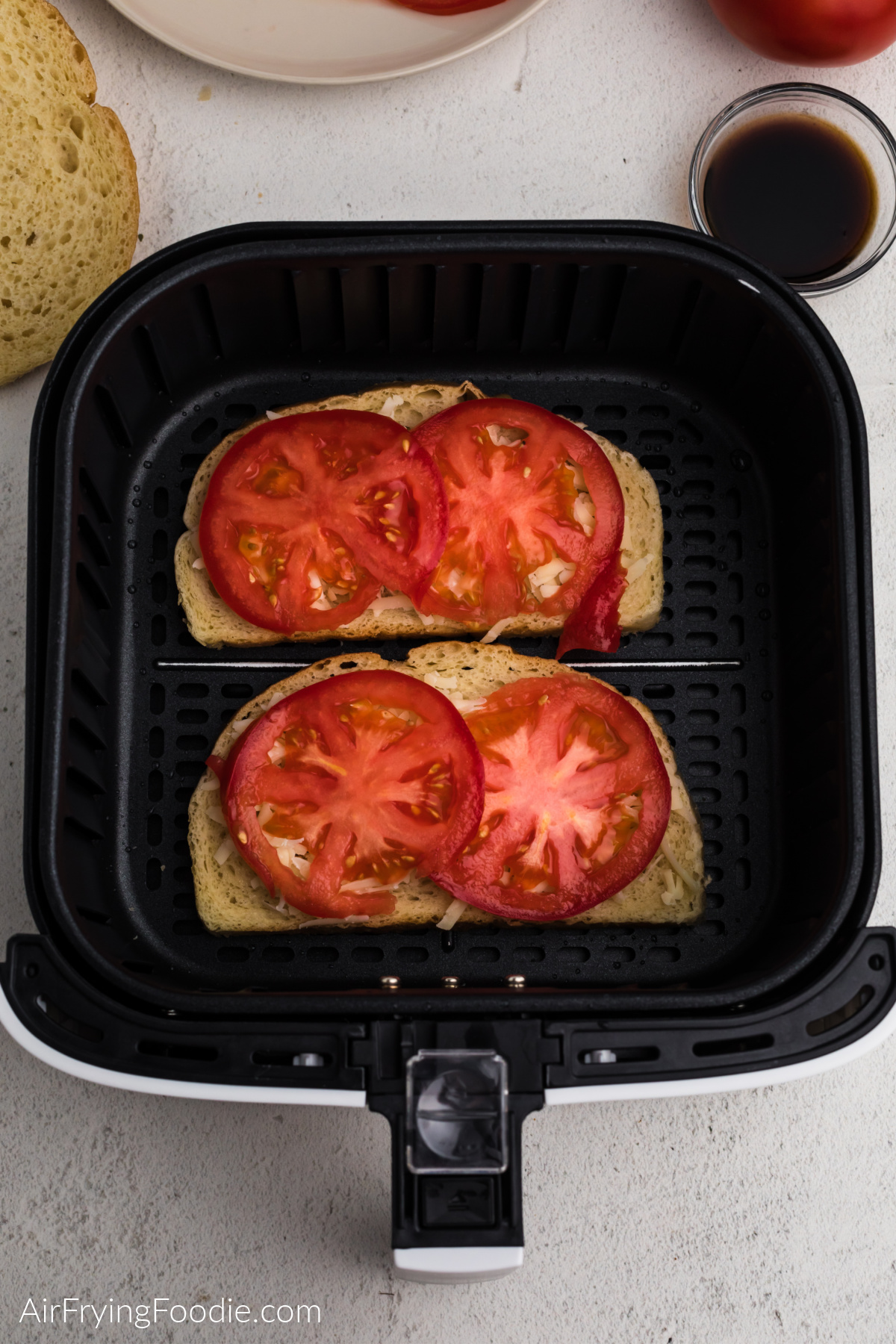 Cheese and sliced tomatoes on sourdough bread in the air fryer basket.