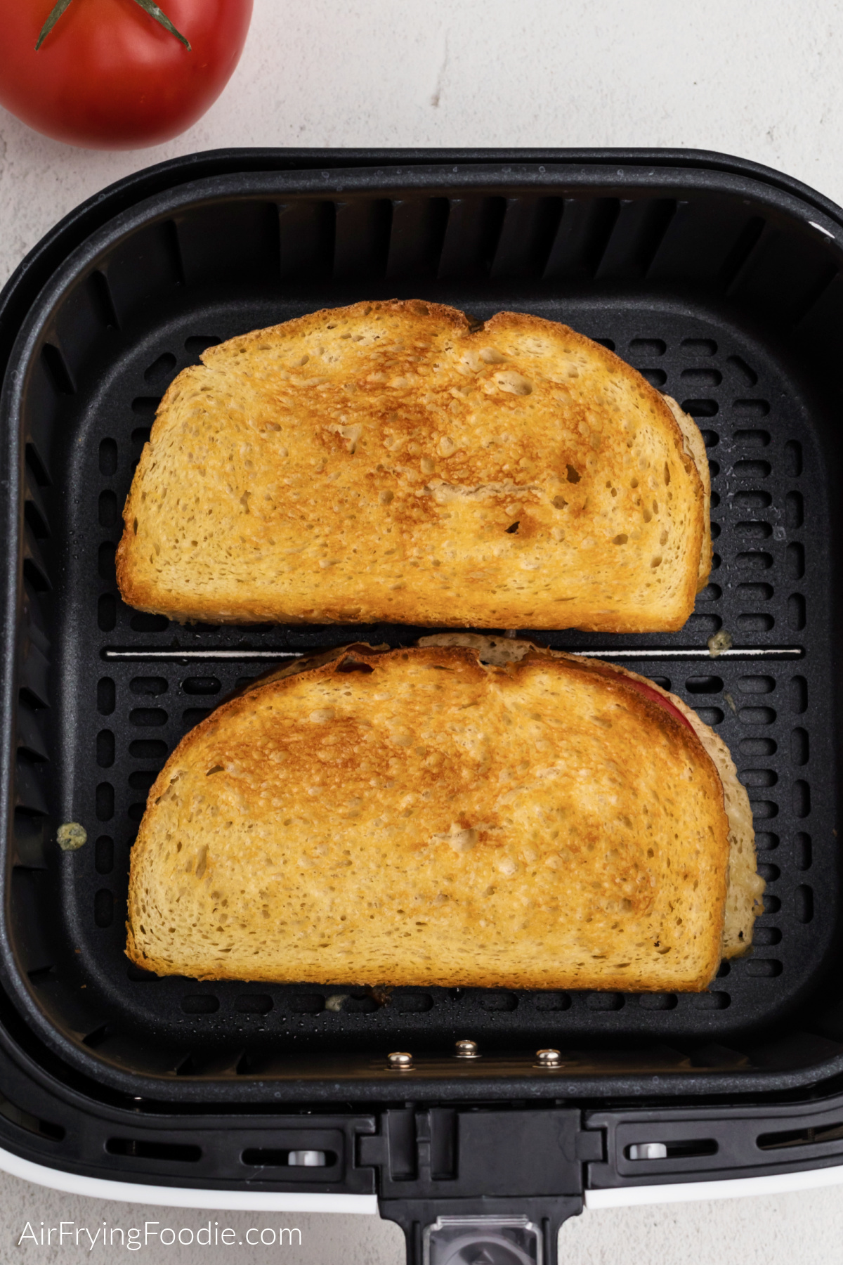 Grilled tomato and cheese sandwich in the basket of the air fryer.