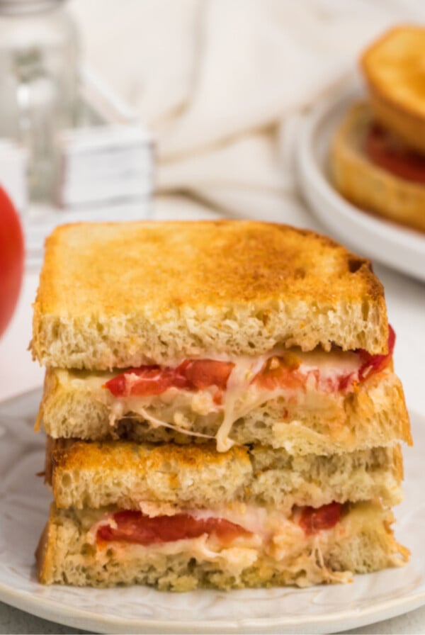 Sliced and stacked grilled tomato and cheese sandwich made in the air fryer and served on a white plate.