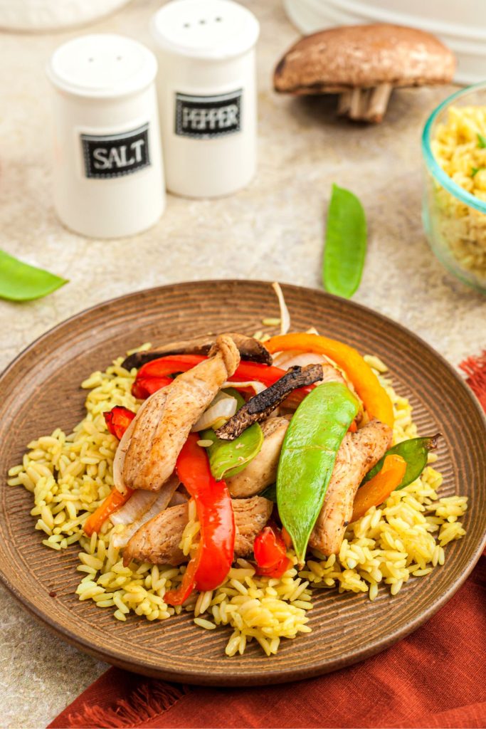 Chicken stir fry served over rice on a light brown plate