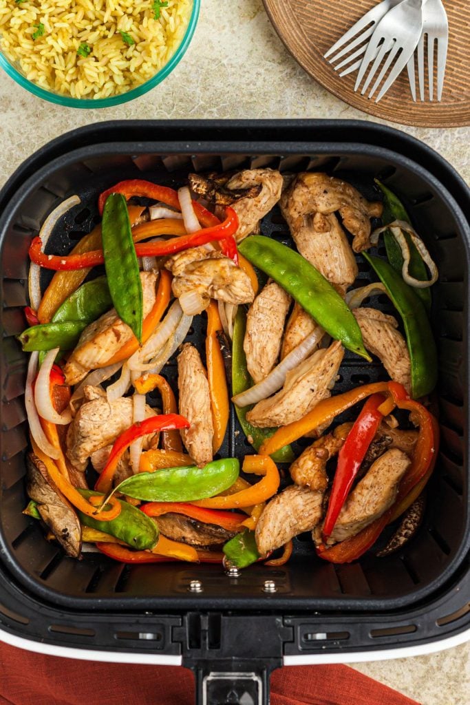 Juicy cooked chicken with stir fry vegetables in the air fryer basket after being cooked
