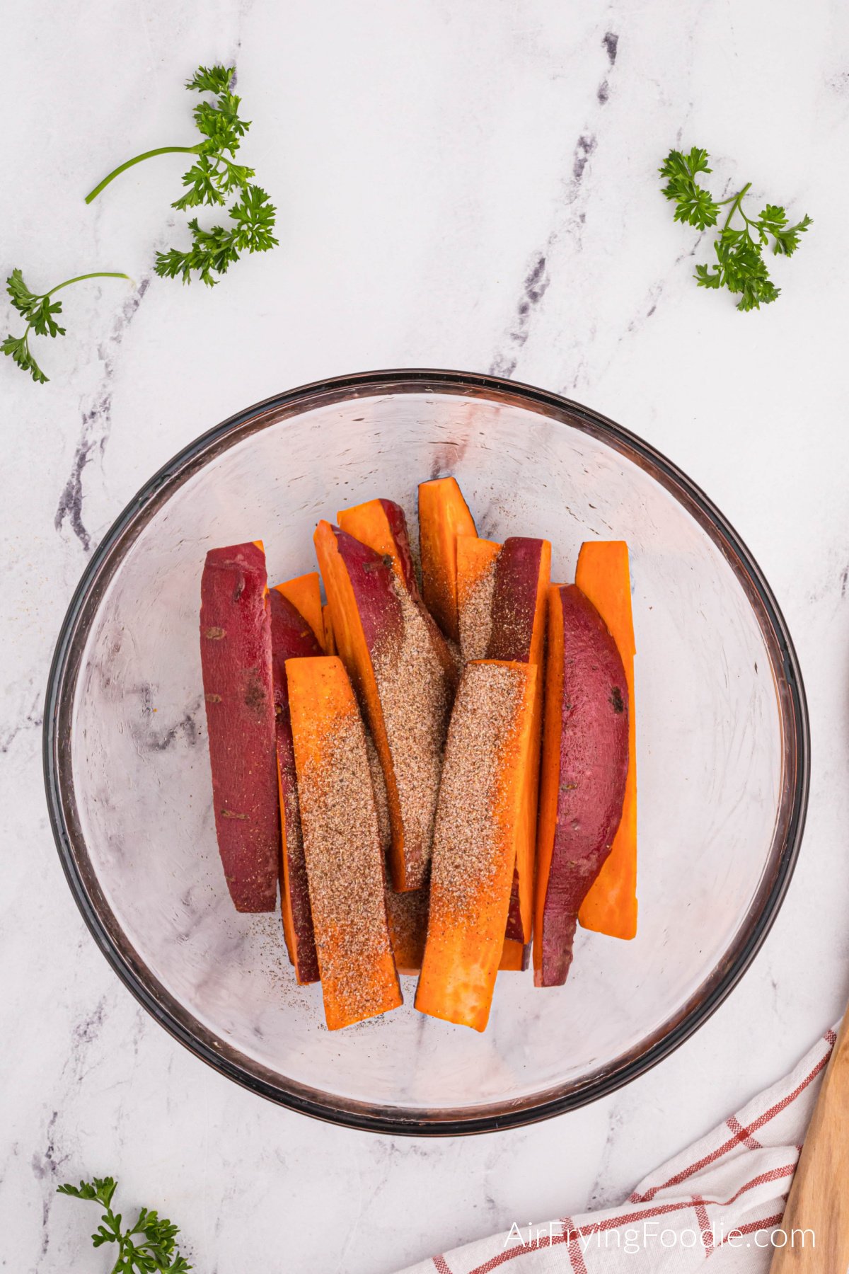 Sweet potato wedges in a bowl with seasonings added to them.