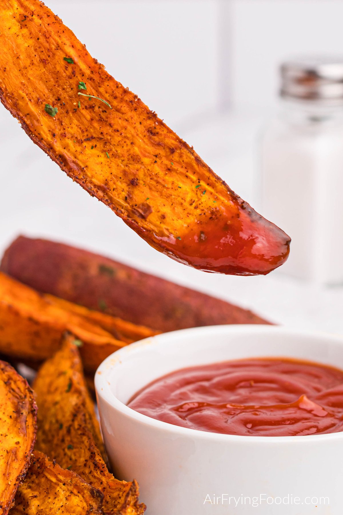 Close up of an air fried sweet potato wedge being dipped into ketchup.