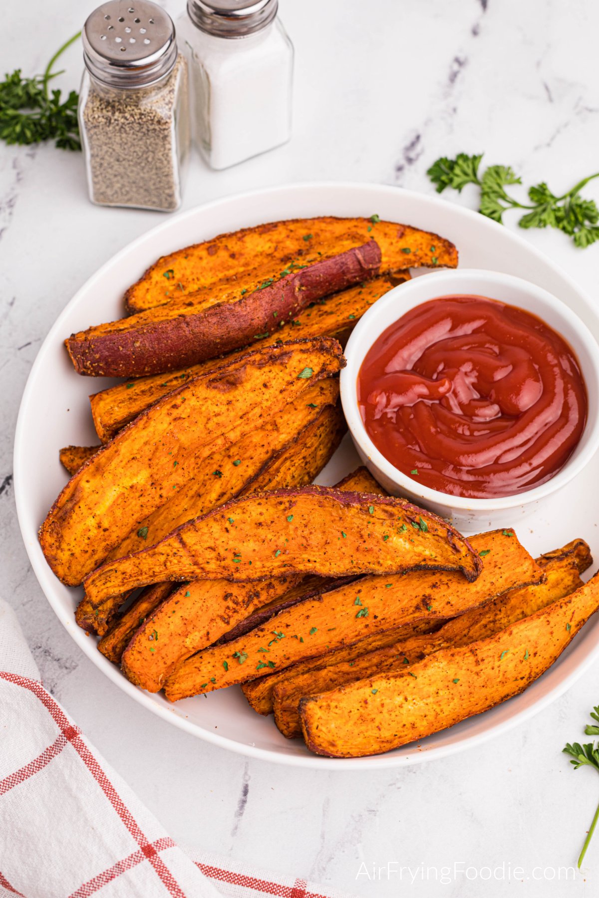 Overhead photo pf air fried sweet potato wedges with a small bowl of ketchup, on a white plate, ready to serve.