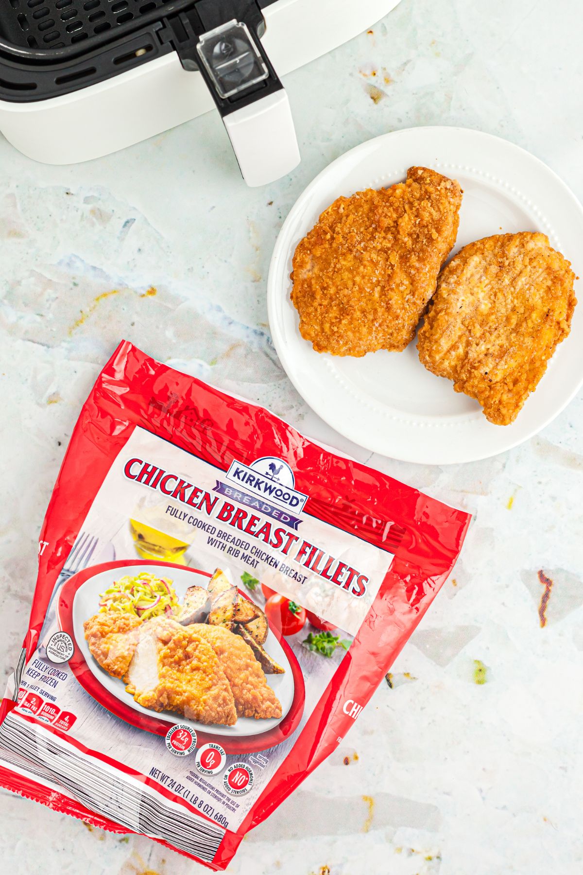 Aldi's Legendary Red Bag Chicken 3 Close-up of the red bag of Kirkwood breaded chicken breast fillets with a cooked chicken fillet on a white plate, set against a marble countertop.