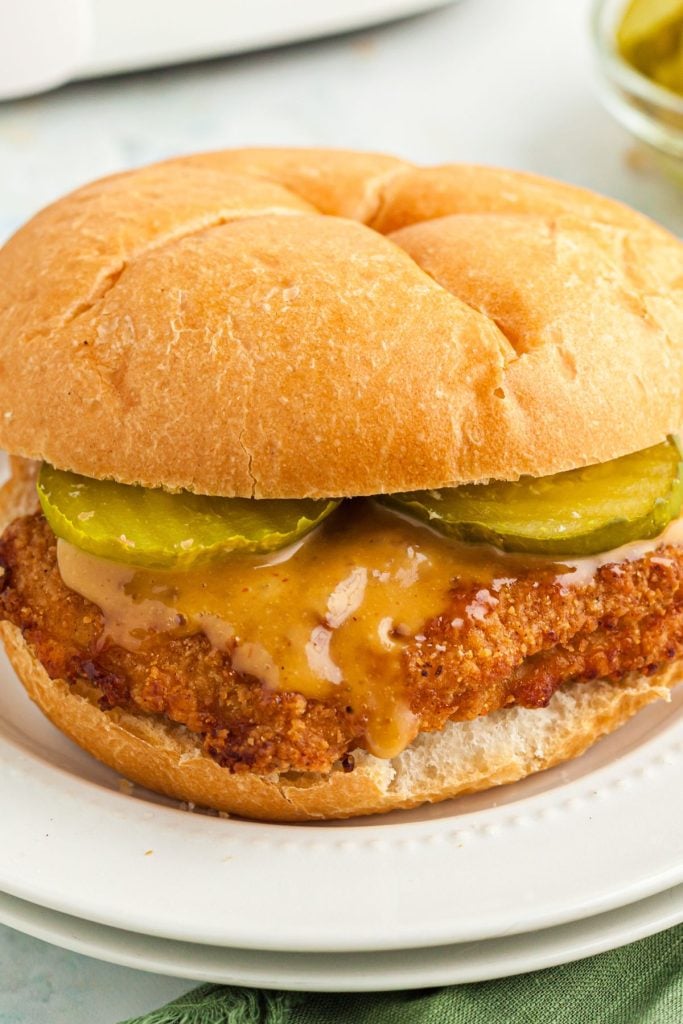 Golden chicken breast in buns with sauce and pickles.