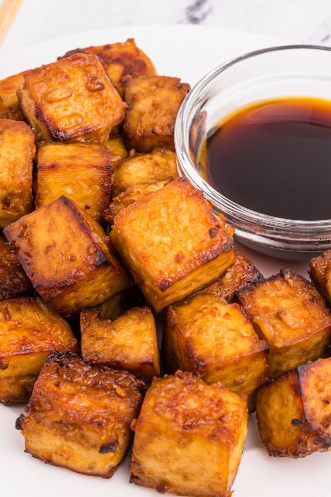 Golden crispy tofu cubes on a white plate with soy sauce