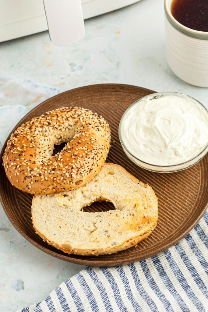 Lightly toasted bagels on a brown plate with a small bowl of cream cheese