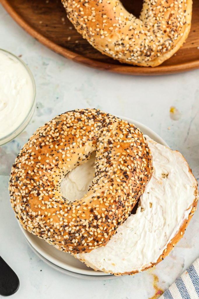 Lightly toasted bagels with seasonings sliced and coated with cream cheese on a small white plate