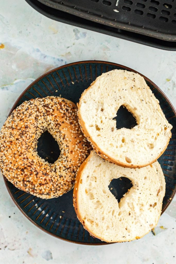 Untoasted bagels on a dark plate in front of air fryer basket