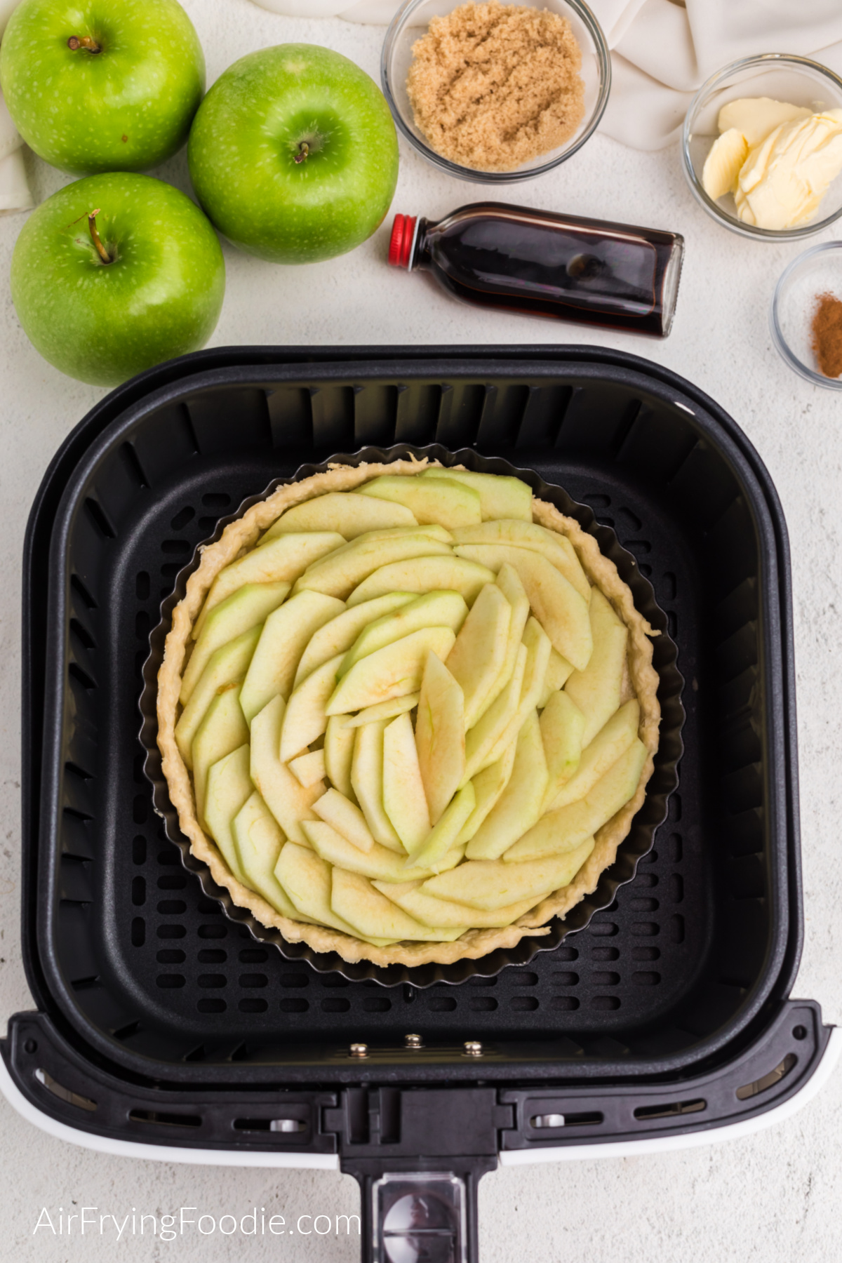 Sliced apples arranged ver the pie crust in the tart pan.