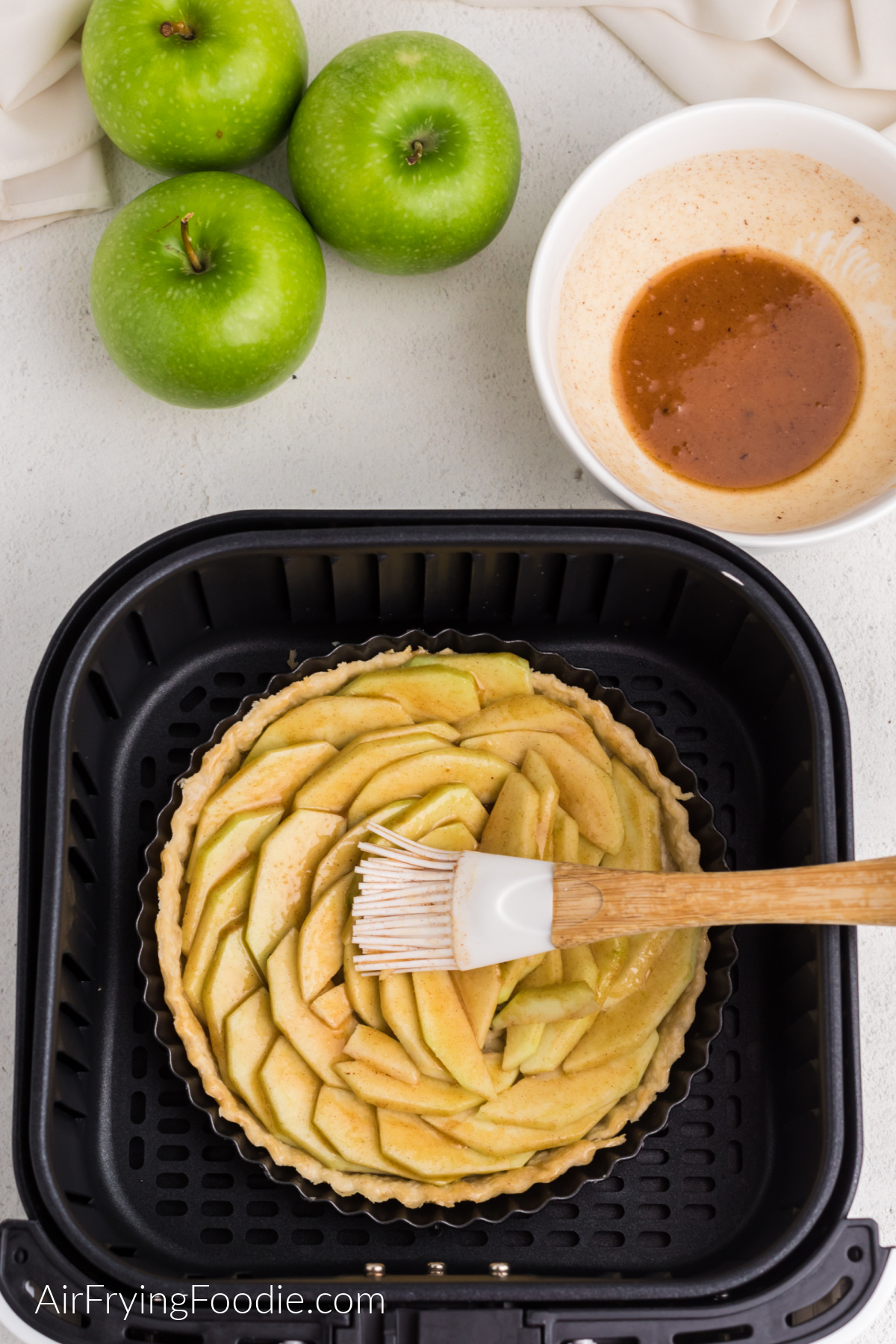 Brushing the top of the apples in the tart with a pastry brush.