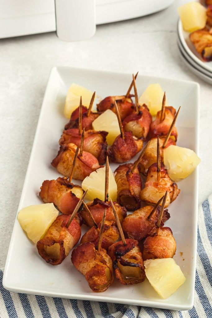 Crispy bacon wrapped pineapple bites on a long white plate in front of the air fryer