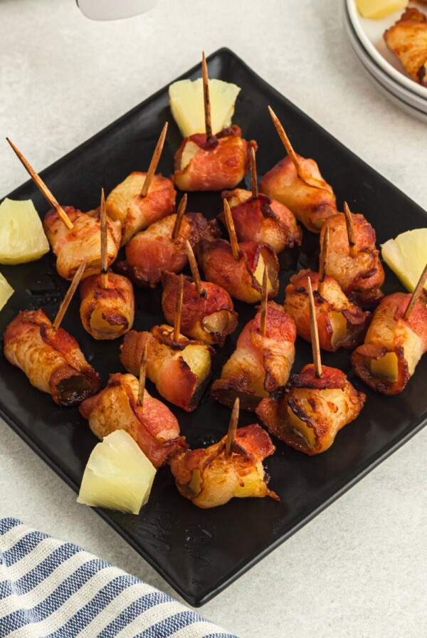 Crispy bacon wrapped pineapple bites on a square black plate