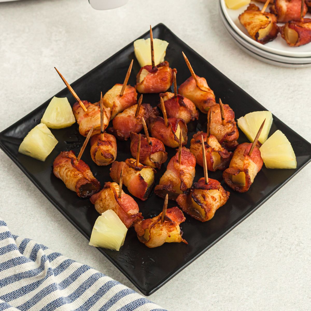 Crispy bacon wrapped pineapple bites on a square black plate