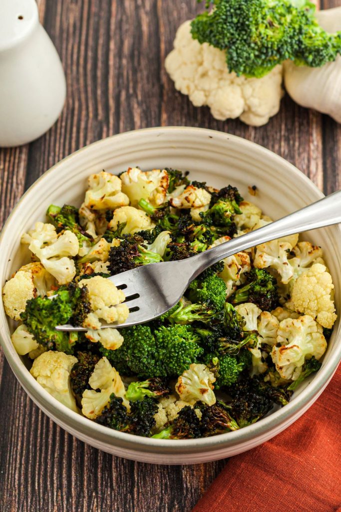 A cream bowl filled with broccoli and cauliflower florets with a fork in the bowl