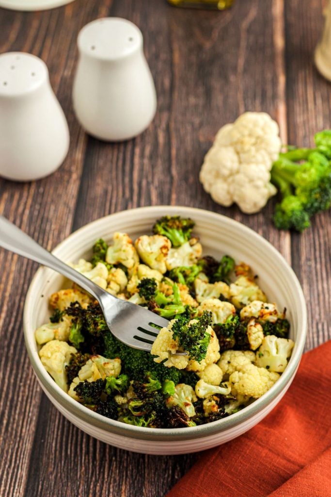 Crispy broccoli and cauliflower in a tan bowl with a fork on a wooden table.