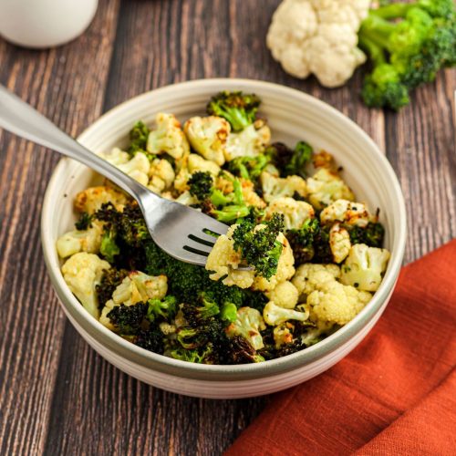 Green broccoli and white cauliflower in a cream bowl on a wooden table