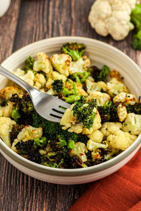 Green broccoli and white cauliflower in a cream bowl on a wooden table