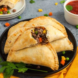 Golden empanadas filled with ground beef and vegetables on a black plate