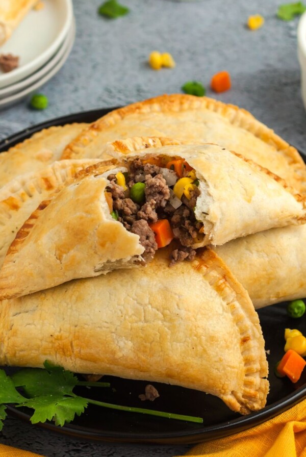 Golden empanadas filled with ground beef and vegetables on a black plate