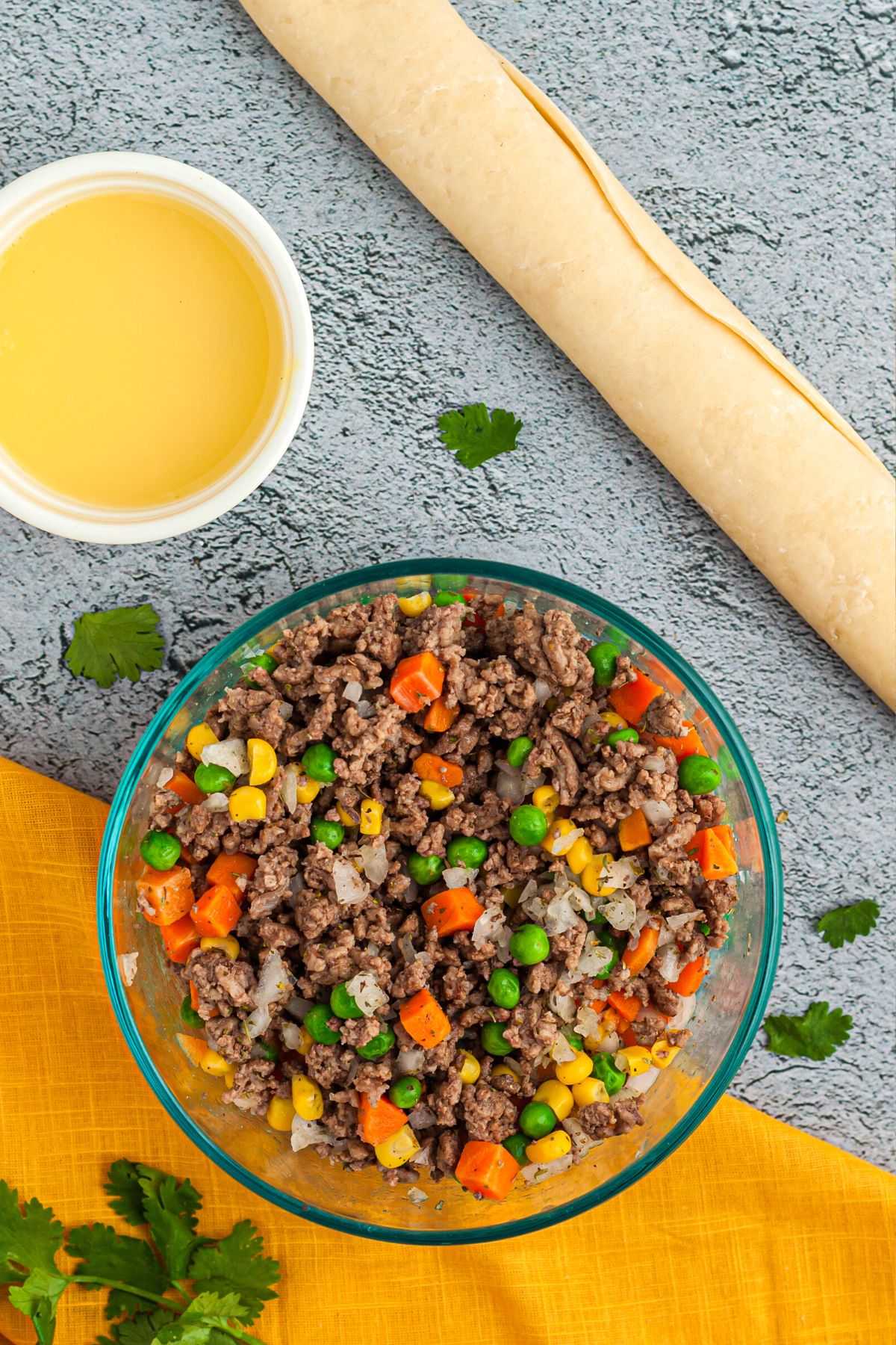 Ground beef mixed with vegetables in a clear glass bowl on a light blue table