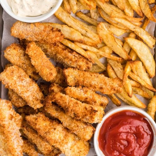 Fish and chips on a baking sheet with ketchup and dipping sauce.