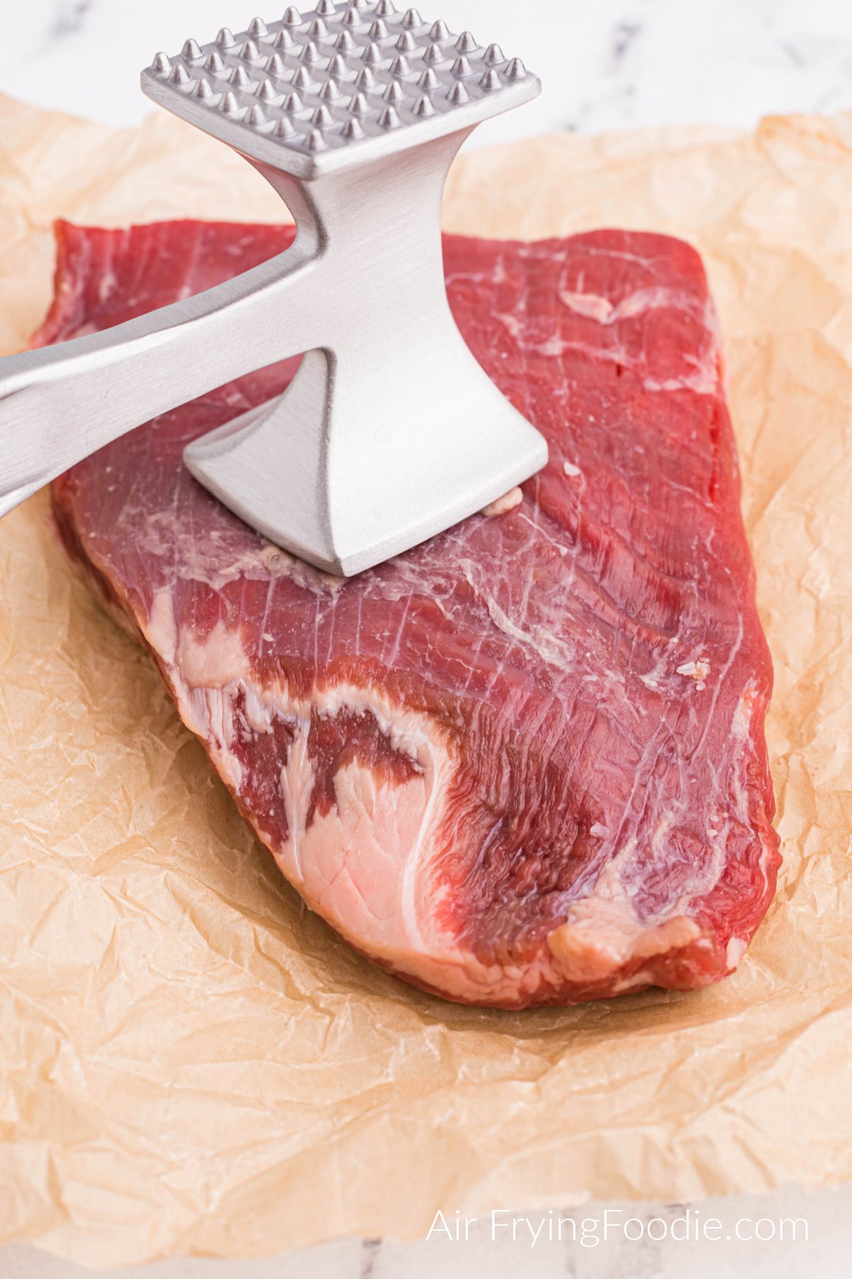 Steak being tenderized with a meat mallet.