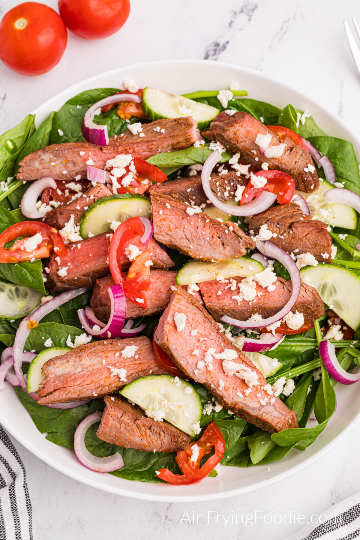 Air fried flank steak on a platter with salad fixings for a steak salad. 