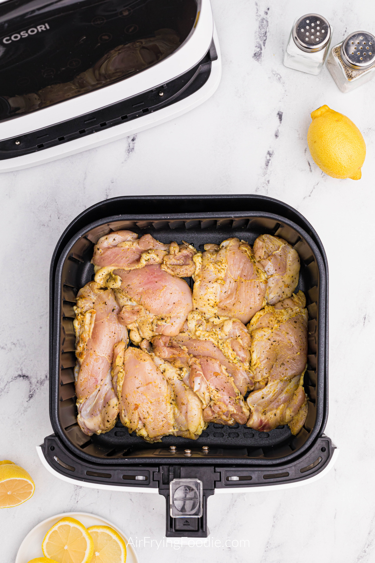 seasoned lemon pepper chicken thighs in the basket of the air fryer.