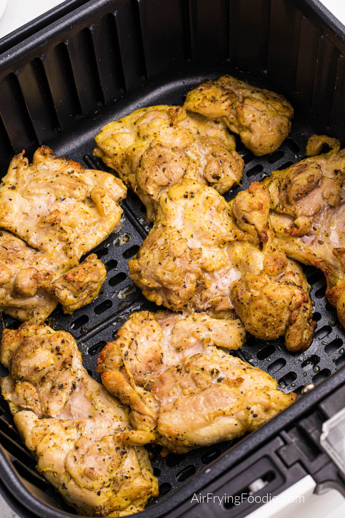 Seasoned lemon pepper chicken thighs in the basket of the air fryer, fully cooked and ready to serve.